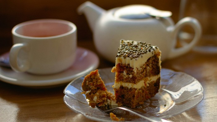 Ein Stück Kuchen auf einem Teller mit einer Tasse Tee und einer Teekanne.