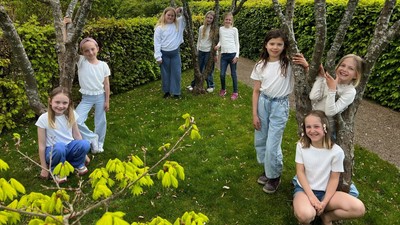 En gruppe glade børn, der leger og poser mellem veltrimmede træer og grønt græs.