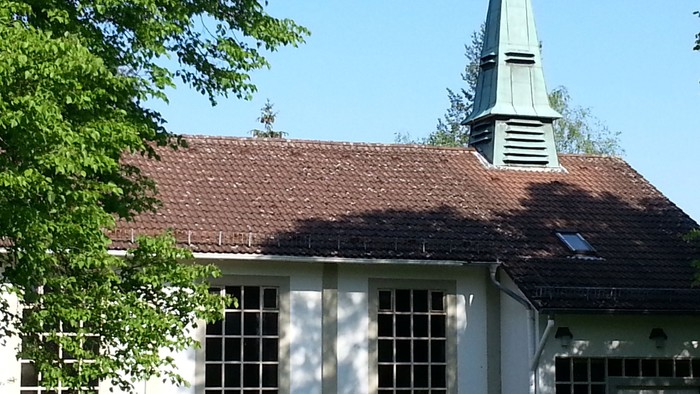 Kleine weiße Kirche mit rotem Dach und hohem Turm auf grünem Rasen.