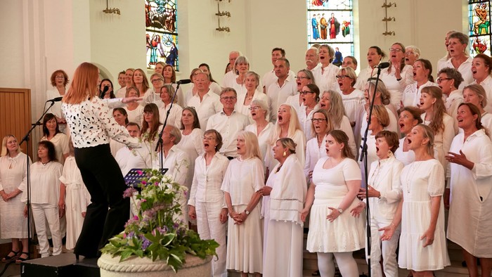 En kor ledet af en kvinde i sort og hvid, synger i en kirke.