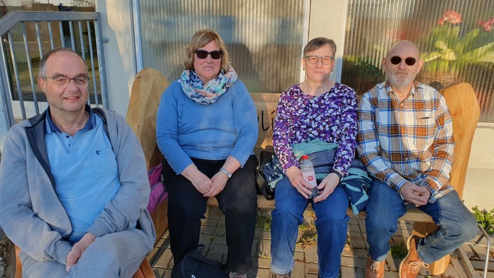 Vier Personen sitzen auf Stühlen im Freien, lächeln und posieren für ein Foto.