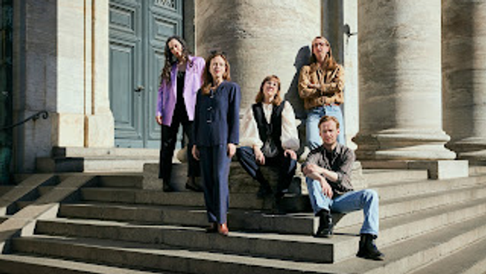 En gruppe på fem personer, der poser på store stentrapper foran indgangen til en klassisk bygning.