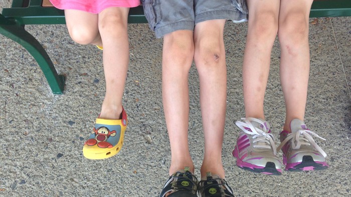 Tre børn sidder på en bæn og viser deres sko.