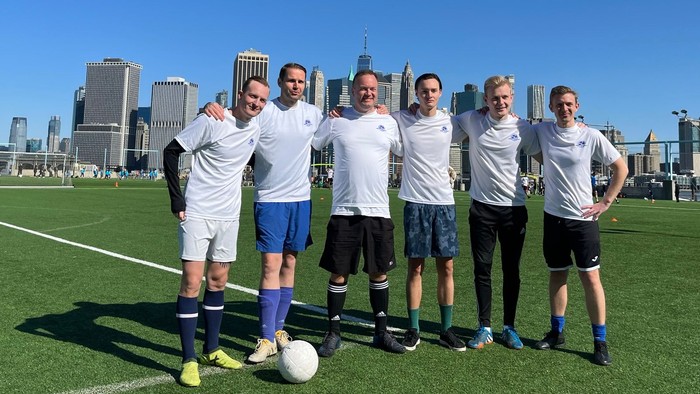 En gruppe fodboldspillere poserer på et græsfelt med byskyline i baggrunden
