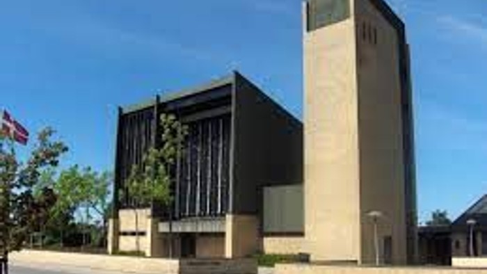 Et moderne bygning med en stor vinduesfront og en flagstang med flag.