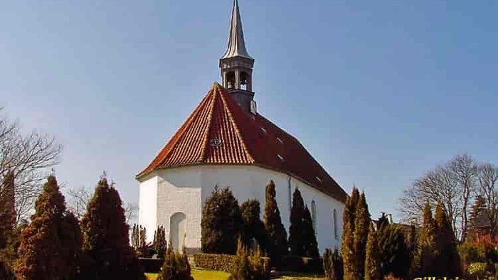 En hvid kirke med rødt tag og spir med kryds i en parkagtig omgivelse