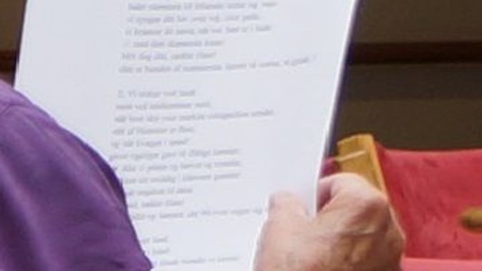 En person holder et papir med en tekst på, mens de sidder ved et bord.