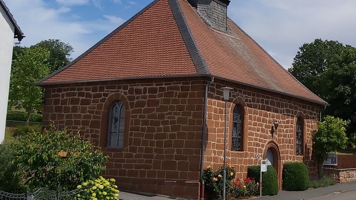 Kleine Backsteinkirche mit rotem Dach und Glockenturm.