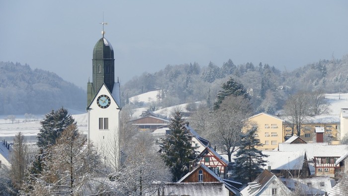 Weißer Kirchturm mit Uhr in verschneitem Dorf