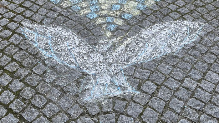 Ein Vogel aus weißen Steinen auf Kopfsteinpflaster.