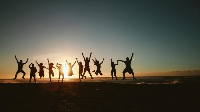 Eine Gruppe von Menschen springt freudig am Strand bei Sonnenuntergang.