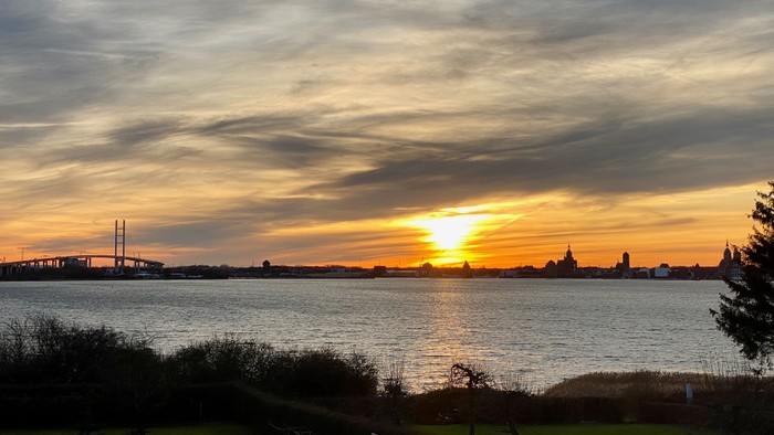 Ein wunderschöner Sonnenuntergang über einem ruhigen Gewässer mit Brücke und Bäumen im Vordergrund