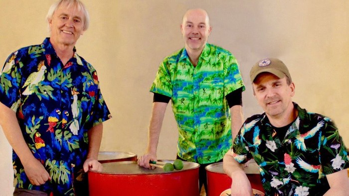 Tre mænd i farverige blomstrede skjorter poser med forskellige percussioninstrumenter og smiler.