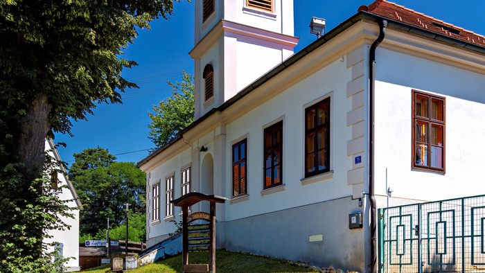 Weiße Kirche mit Uhrturm und rotem Dach, umgeben von Bäumen und Gras.