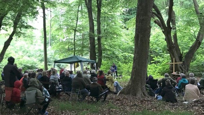 En gruppe af mennesker sidder på stolene i skoven og lytter til en tale.