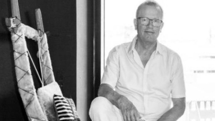 Studie-Sort/hvidt foto af Christian Søgaard, der sidder i hvidt tøj med korte ærmer på en hundeslæde, tromme med ornamentik i forgrunden, vindue i baggrunden