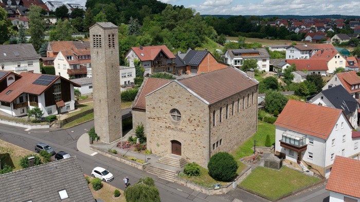 Ein Dorf mit Kirche und Wohnhäusern, umgeben von Grünflächen und Autos auf der Straße.
