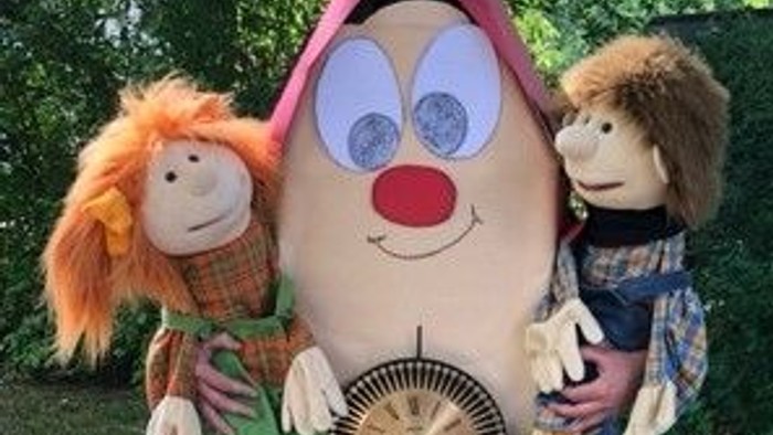 Zwei Puppen stehen vor einer großen Uhr mit Clowngesicht.