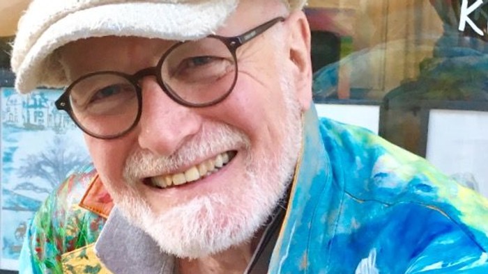 Mand med et smil poser glad i en farverig tie-dye-jakke og kasket uden for en butik.