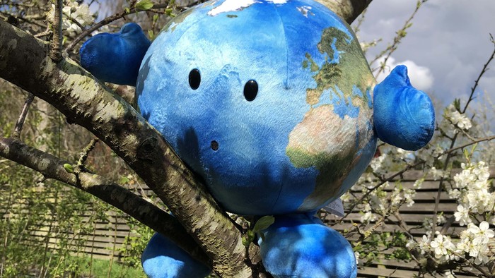 En blå globus med ansigtsfødder og øjne hænger i et træ.