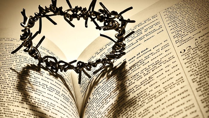 Eine offene Bibel mit einer Dornenkrone, die einen herzförmigen Schatten auf ihre Seiten wirft.