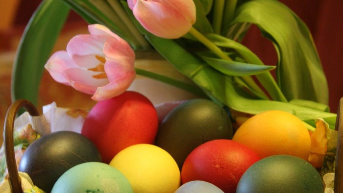 Ein Korb mit bunt gefärbten Ostereiern und einer Blume