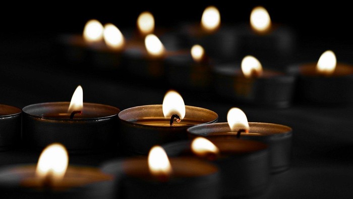 Eine Sammlung brennender Kerzen, die warmes, flackerndes Licht auf einen dunklen Hintergrund werfen.