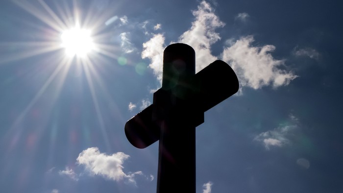 Ein Kreuz vor einem sonnenstrahl durchzogenen Himmel