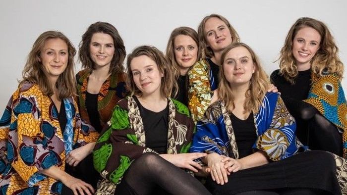 Syv kvinder i farverige jakker sidder sammen og smiler til kameraet