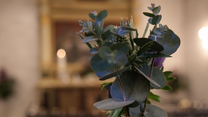 En blomsterstang med blå og grønne blomster i en vase på et bord i en rummelig rom