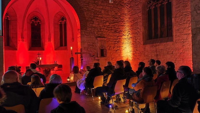 Eine Gruppe von Menschen sitzt in einer Kirche bei Kerzenschein.
