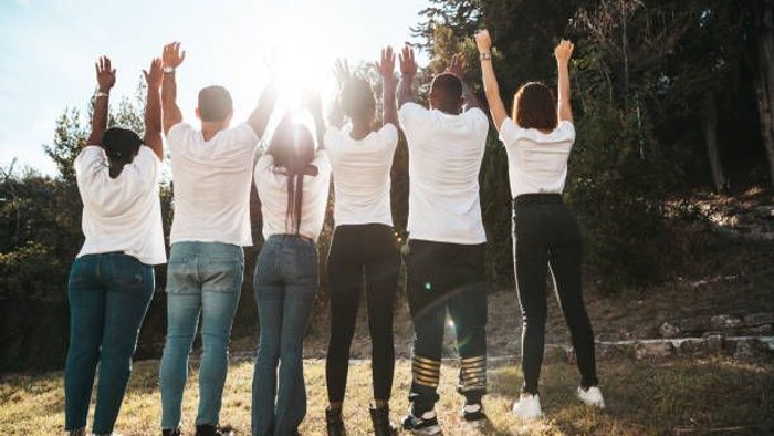 En gruppe mennesker, der glædesfyldt løfter armene op udendørs i naturskønne omgivelser.