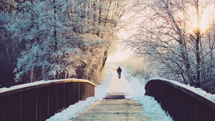 Weg führt über eine Brücke im Schnee, im Hintergrund Bäume und ein Mann in der Ferne