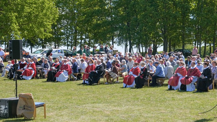 En stor gruppe af personer i røde og hvide uniformer sidder på græs under træer
