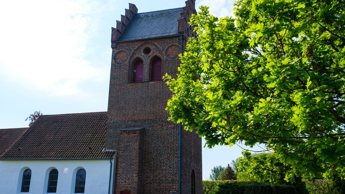 En kirke med tårn og bjærge tak, omgivet af grønne træer og en klar himmel