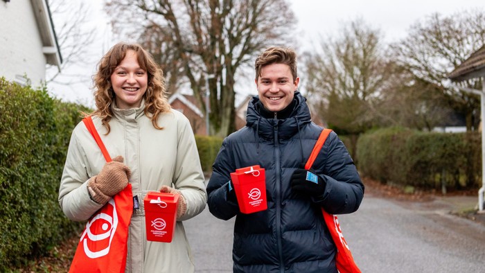 To glade mennesker holder røde kaffekopper og poser på en boligvej.