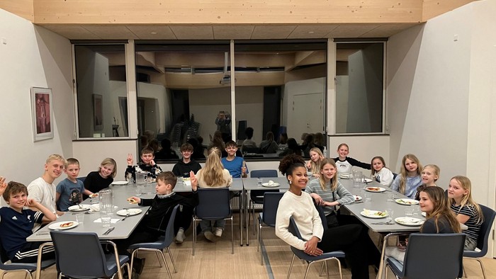 En gruppe mennesker, der sidder ved borde i et moderne rum med store vinduer.