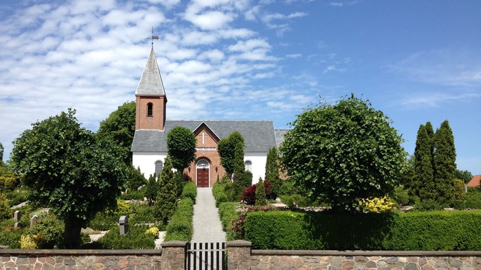 En smuk kirke med tårn og omgivelser af grønne træer og buske