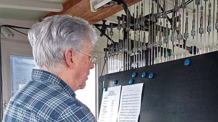 En mand spiller på et indviklet pibeorgel med detaljerede manualer og piber bag sig.