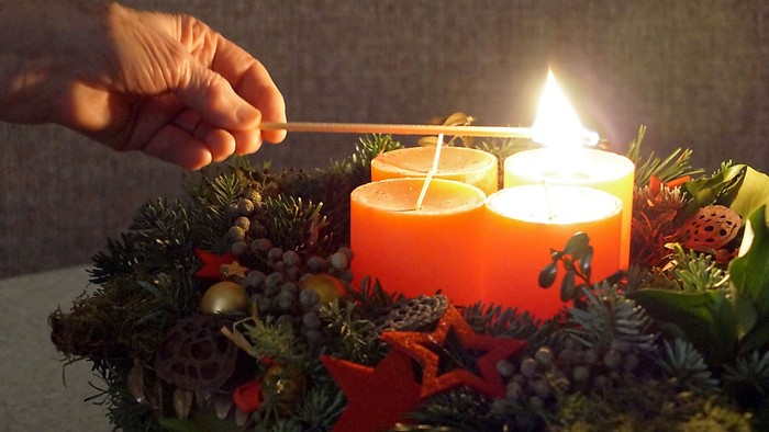 Eine Hand zündet Kerzen auf einem Adventskranz an