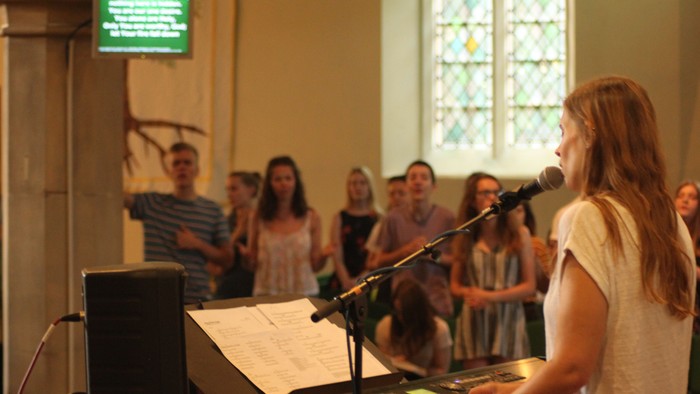 Woman singing into microphone with group behind her