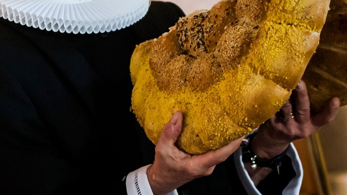 En person holder et stort, gyldenbrunt brød med en smuldrende top.