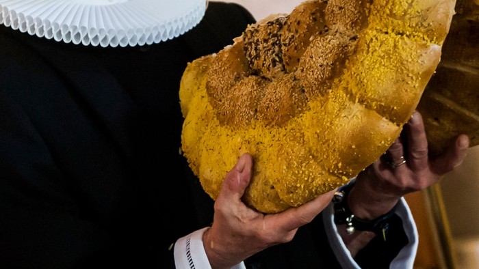 En person holder et stort, gyldenbrunt brød med en smuldrende top.