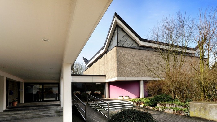 Modernes Gebäude mit schrägem Dach und pinkfarbenem Innenraum, der durch offene Türen sichtbar ist