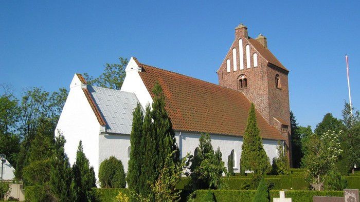 Et hvidt kirkebygning med røde tag og en tårn med klokke.