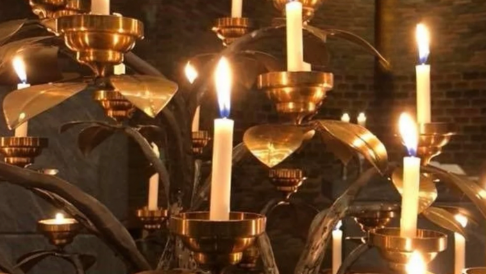 Flere tændte stearinlys i udsmykkede lysestager, sandsynligvis i en kirke eller religiøs sammenhæng.