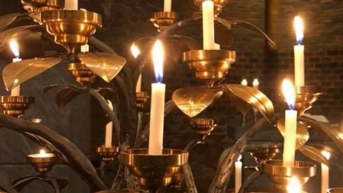 Flere tændte stearinlys i udsmykkede lysestager, sandsynligvis i en kirke eller religiøs sammenhæng.