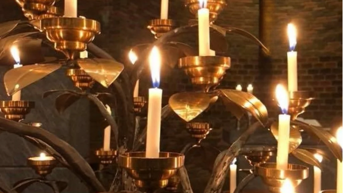 Flere tændte stearinlys i udsmykkede lysestager, sandsynligvis i en kirke eller religiøs sammenhæng.