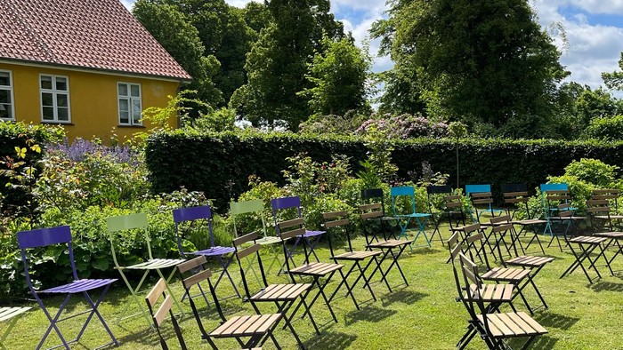 Udehuse med bord og stole i træ og metal i en have med blomster og græs