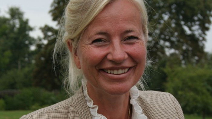 En kvinde med blond hår og en blå blazer smiler til kameraet.